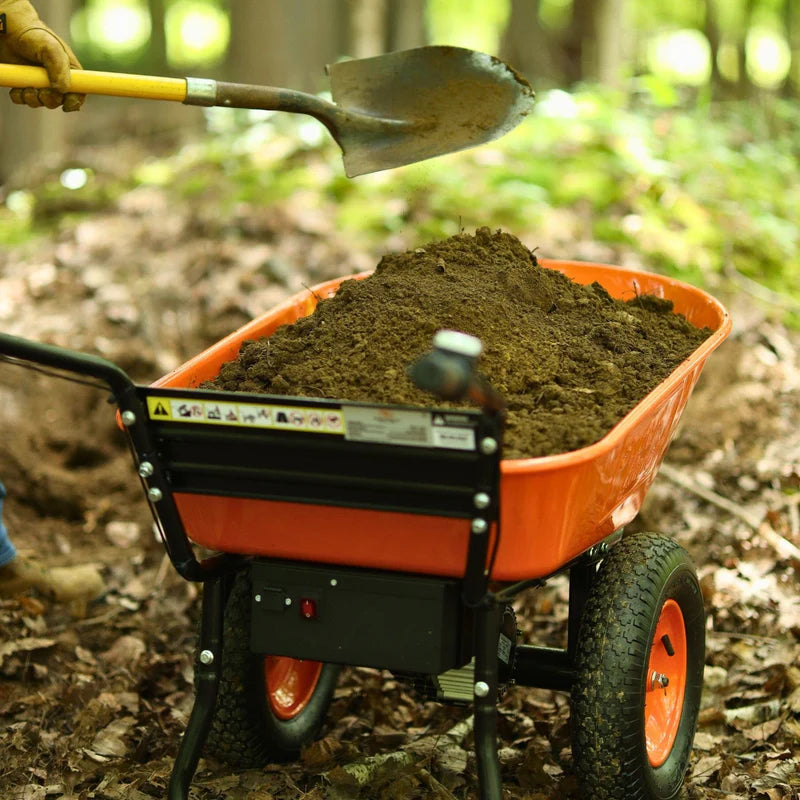 An orange and black superhandy 24v  electric wheelbarrow with a visible 24V 7Ah AGM battery. Back top view outdoors in use.