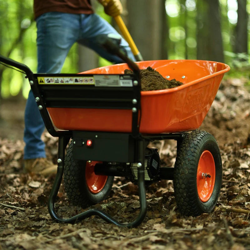 An orange and black electric dualie wheelbarrow with a visible 24V 7Ah AGM battery. Handle view outdoors in use.
