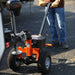 An orange and black SuperHandy Electric Trailer Dolly with all-terrain tires, a powerful electric motor, and a height-adjustable hitch. Front view outdoors in use.