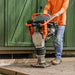 A jumping jack tamping rammer with a 7HP 209CC engine, predominantly black and orange in color, designed for soil compaction. Front view outdoors in use.