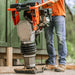 A jumping jack tamping rammer with a 7HP 209CC engine, predominantly black and orange in color, designed for soil compaction. Front view outdoors in use.