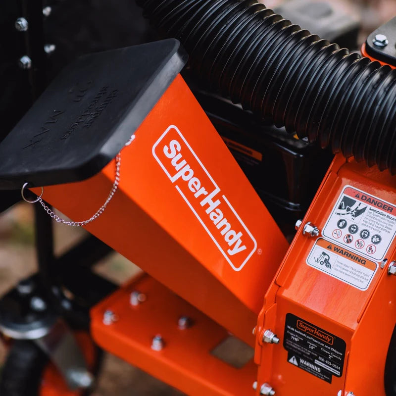 An orange and black gas powered leaf vacuum and wood chipper with a black collection bag and wheels for mobility. Top view outdoors with logo showing.