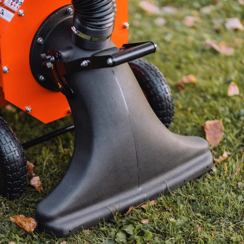An orange and black gas powered leaf vacuum and wood chipper with a black collection bag and wheels for mobility. Wheel view outdoors in use.