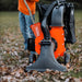 A person operating an orange and gray leaf vacuum and wood chipper in a yard covered with leaves.
