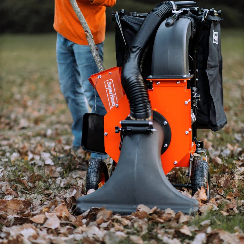 A person operating an orange and gray leaf vacuum and wood chipper in a yard covered with leaves.