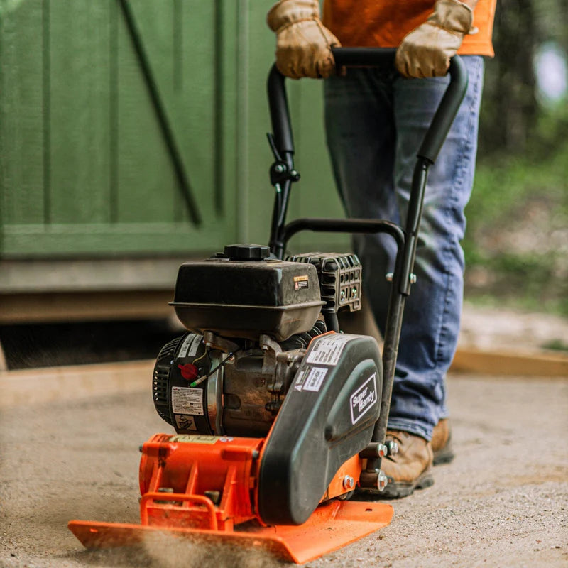 A red and black SuperHandy plate compactor with a gas engine, designed for compacting soil and gravel. Front view outdoors.
