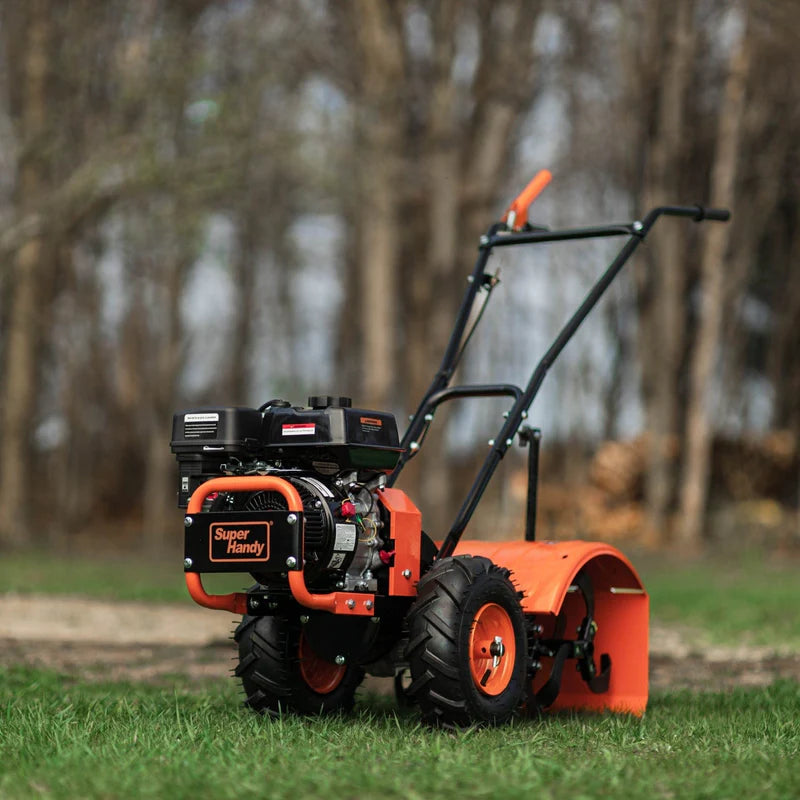 A superhandy rear tine tiller 16" with orange, black, and gray coloring, featuring a gas engine and large wheels for garden soil preparation. Back side view outdoors.