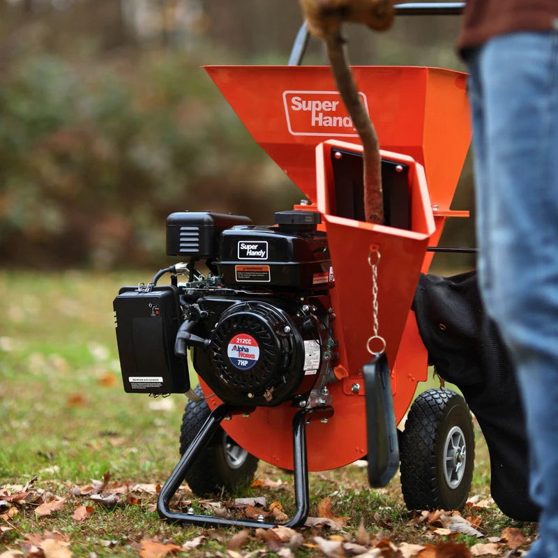 An orange wood chipper with a black cover next to it, featuring a 7HP 212CC engine. Mouth view outdoors in use.