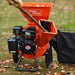 An orange wood chipper with a black cover next to it, featuring a 7HP 212CC engine. Front view outdoors in use.