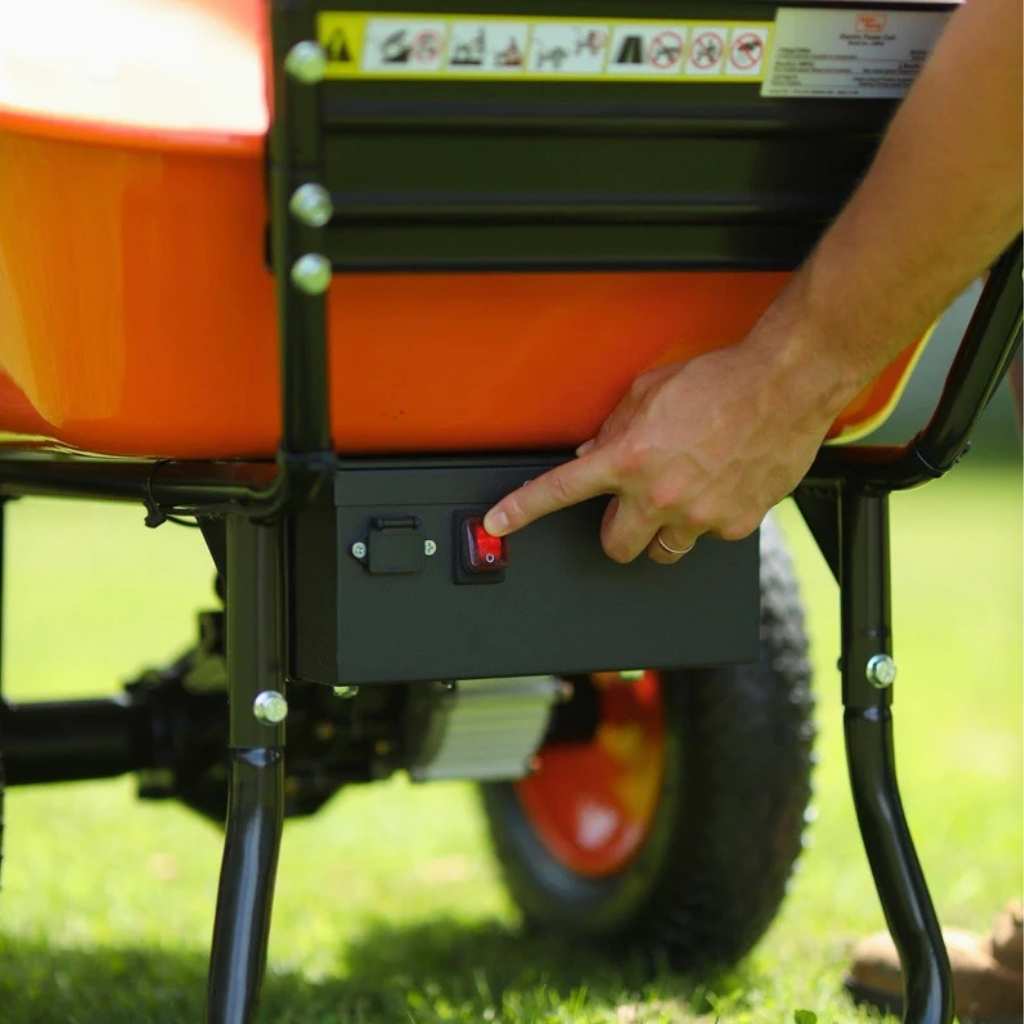 Person pressing a red button on a superhandy 24v battery powered wheelbarrow in a grassy area