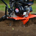 A orange and black superhandy 209cc garden tiller with orange wheels and a 209CC engine. Side front view outdoors in use.