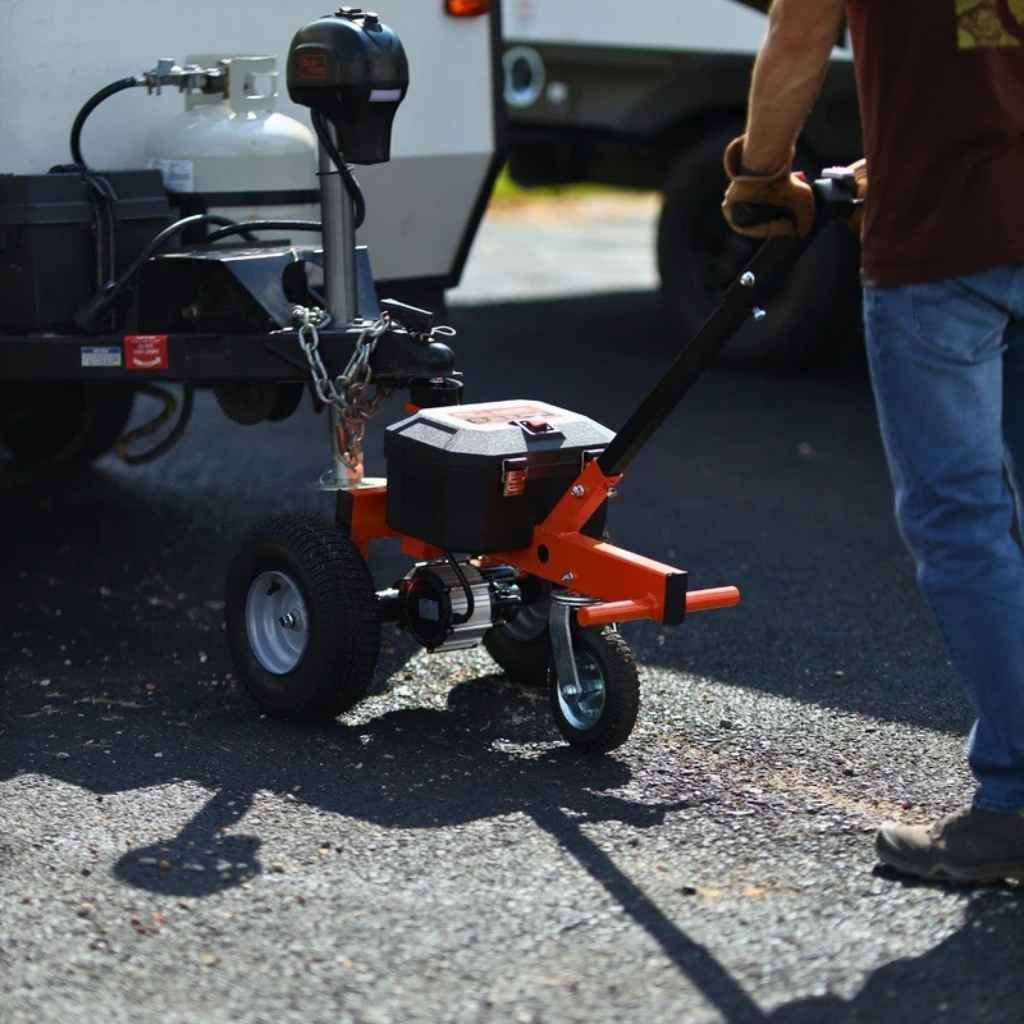 Person using a small orange superhandy 2800 electric dolly on a paved surface with a vehicle in the background.