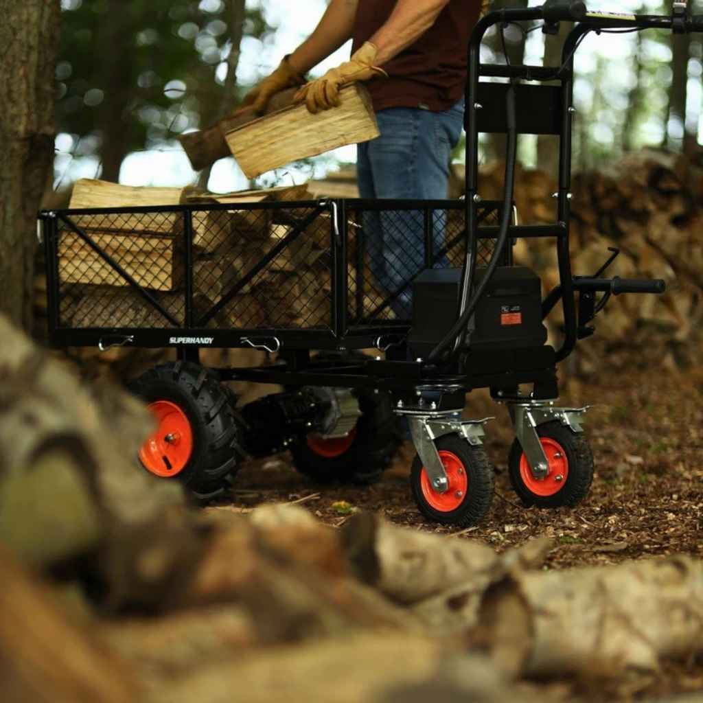 Person pushing a black superhandy utility wagon 48v with red wheels through a forest, carrying wooden planks.