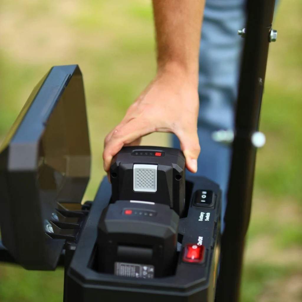 Person attaching a battery pack to a superhandy 48v electric utility wagon outdoors