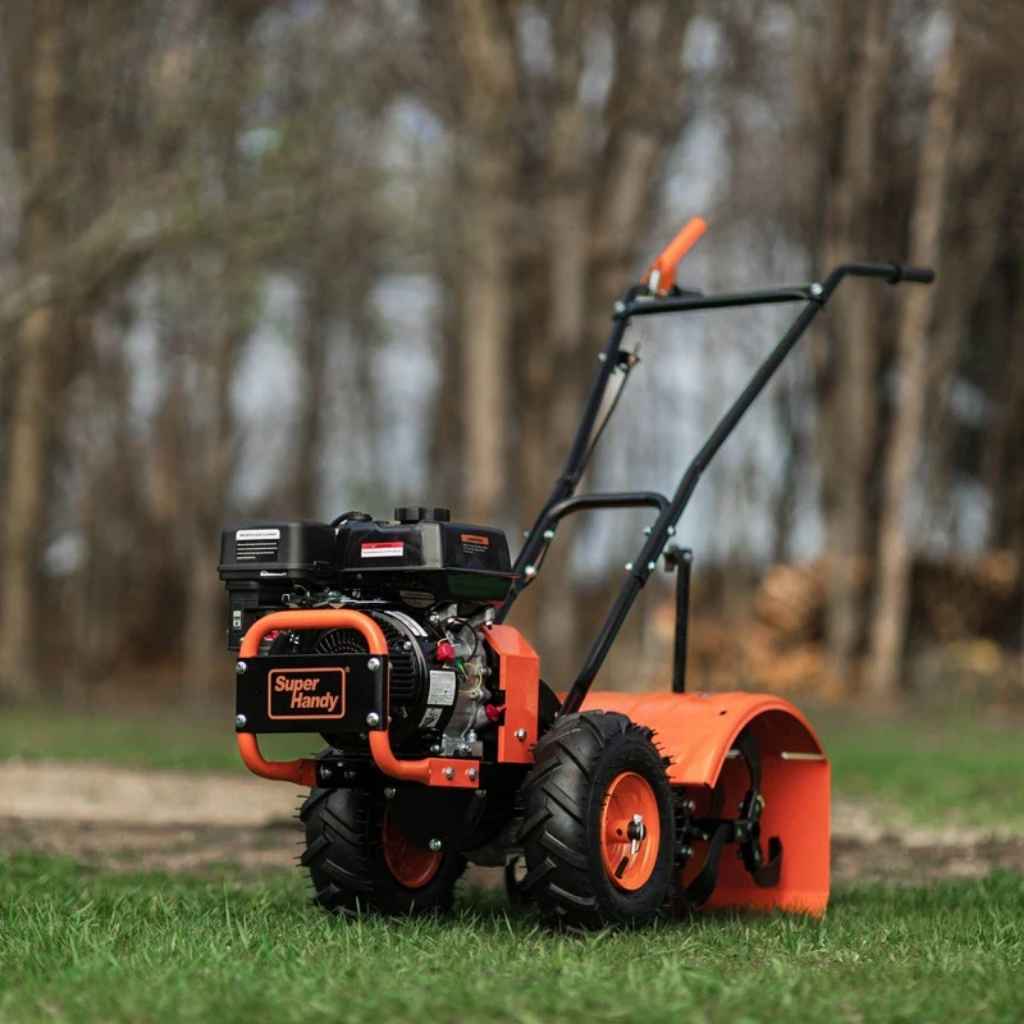 Orange and black superhandy 7hp rear tine tiller on grass with blurred trees in the background