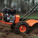 Orange superhandy 16 inch rear tine tiller working in soil with blurred background