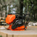 Orange and black superhandy plate compactor with water tank on a wooden surface with a blurred natural background