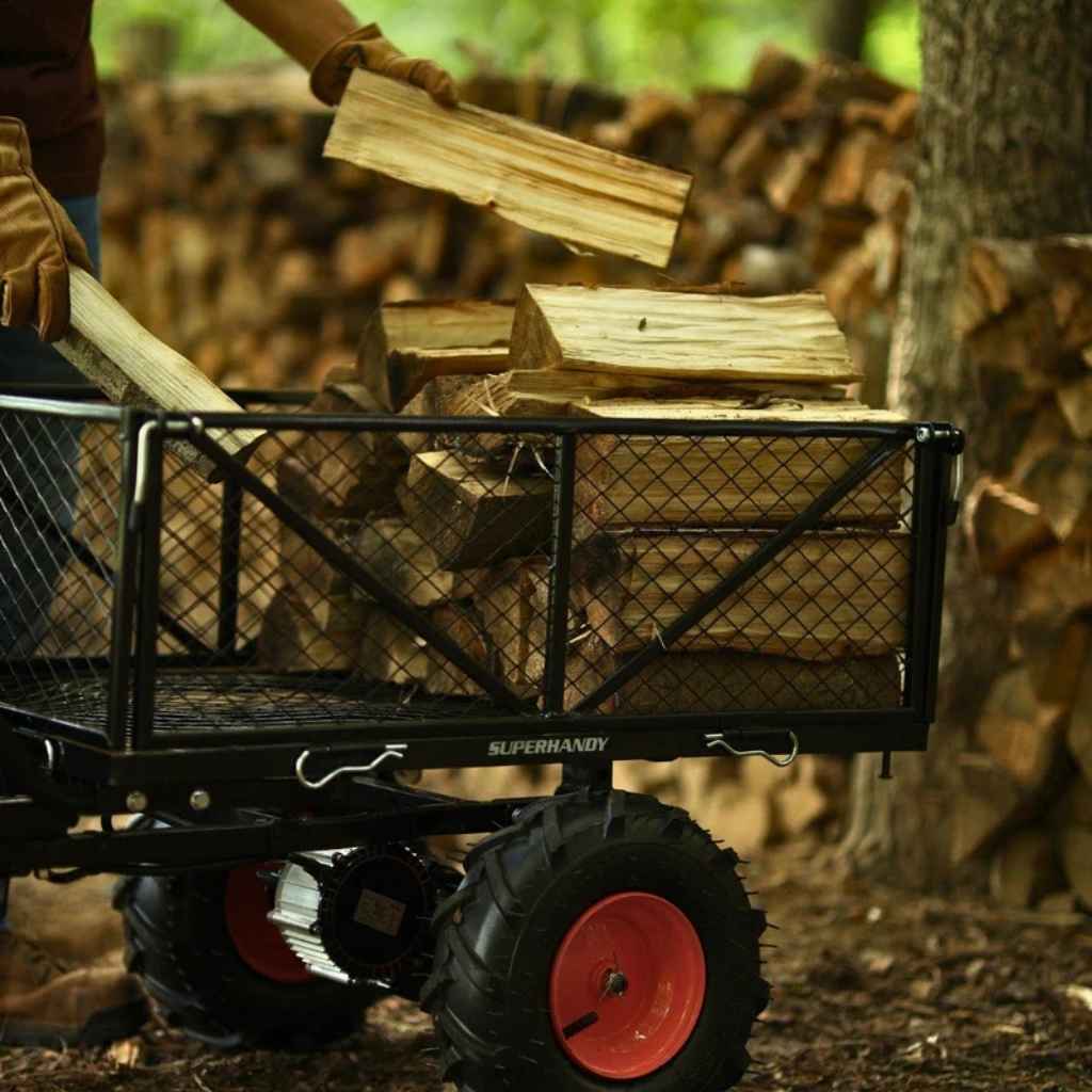 Person loading firewood into a black SuperHandy 48v utility wagon with red wheels in a forest setting.