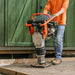Person using a superhandy tamping rammer in front of a green wooden fence