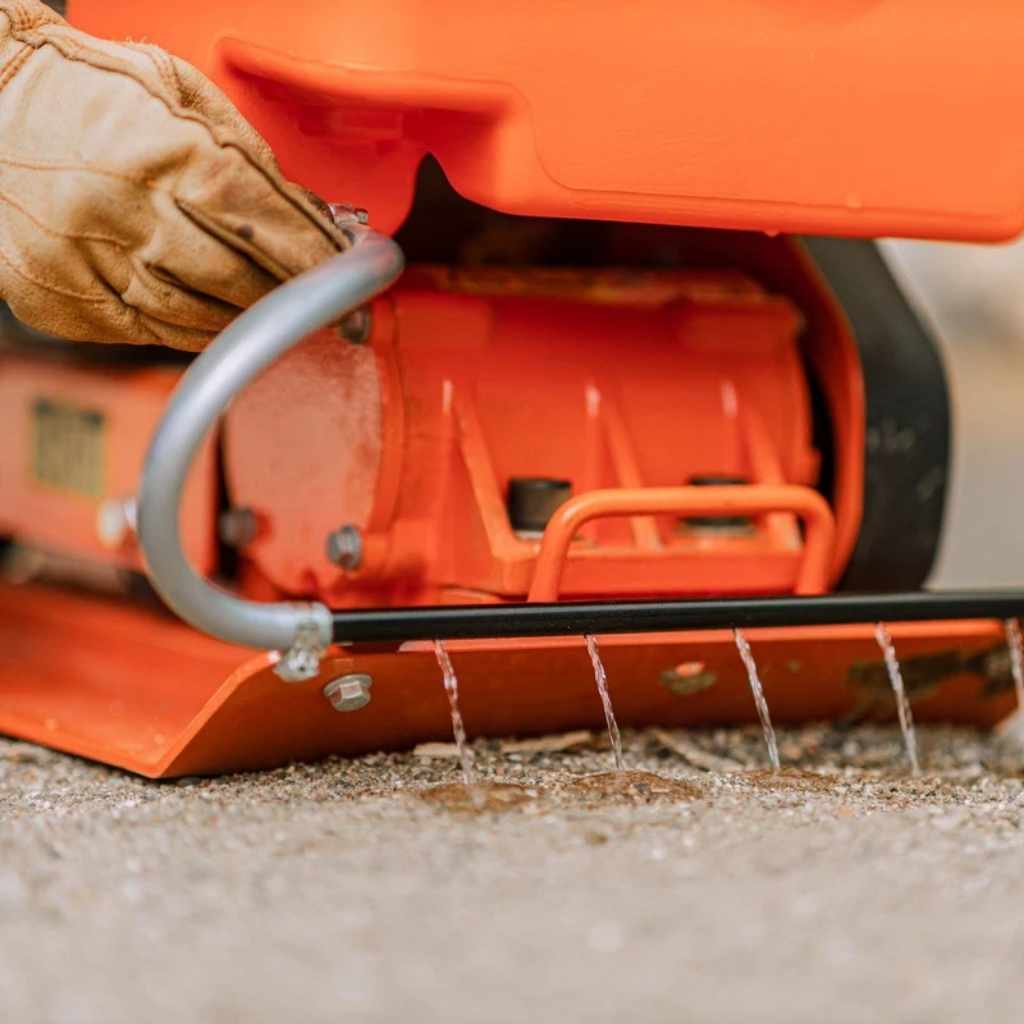 Close-up of a superhandy water tank plate compactor 7 hp in action with a gloved hand, on a concrete surface.