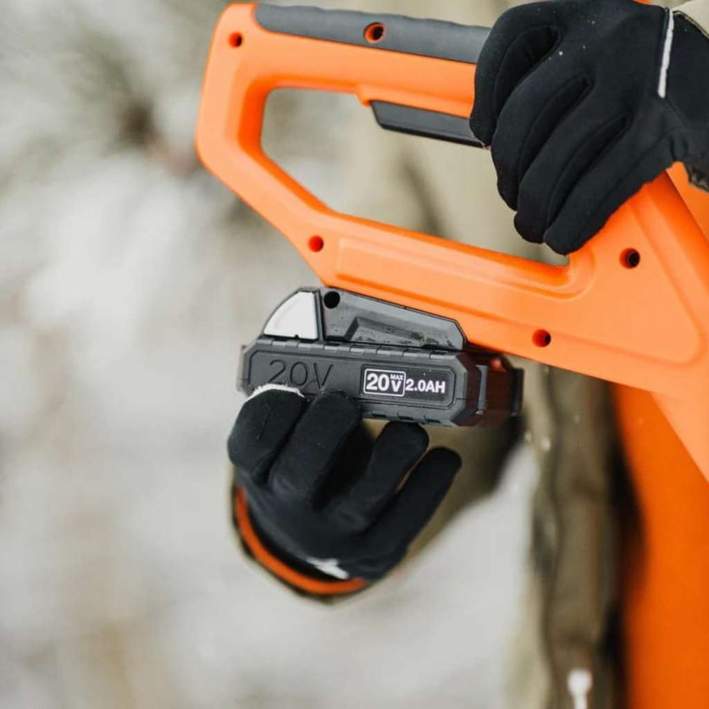 Orange and black superhandy 20v 2 ah snow thrower held by a gloved hand with a blurred background