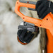 Orange and black superhandy 20v 2 ah snow thrower held by a gloved hand with a blurred background